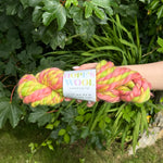 Skein of pink and green yarn held in front of a green leafy background