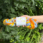 Colorful skein of yarn held by a hand with a green leafy background