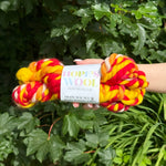 skein of red, yellow, and cream yarn held against a green leafy background