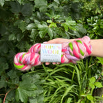 Pink and green skein of yarn held by a hand with a green leafy background