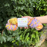 One skein of colourful yarn held by a hand with a 'Hope's Wool' label against a green leafy background.