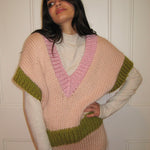 A woman in a pink, cream and green vest standing with a white door