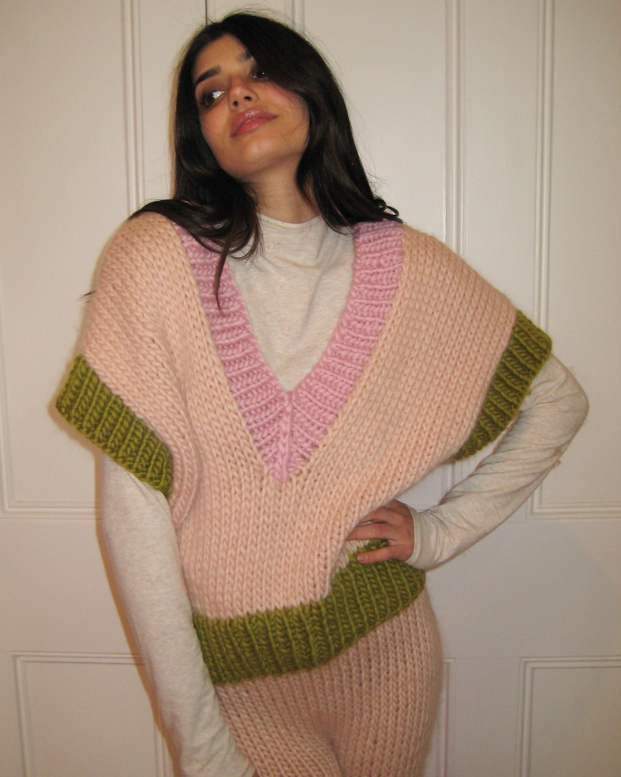 A woman in a pink, cream and green vest standing with a white door