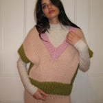 A woman in a pink, cream and green vest standing with a white door