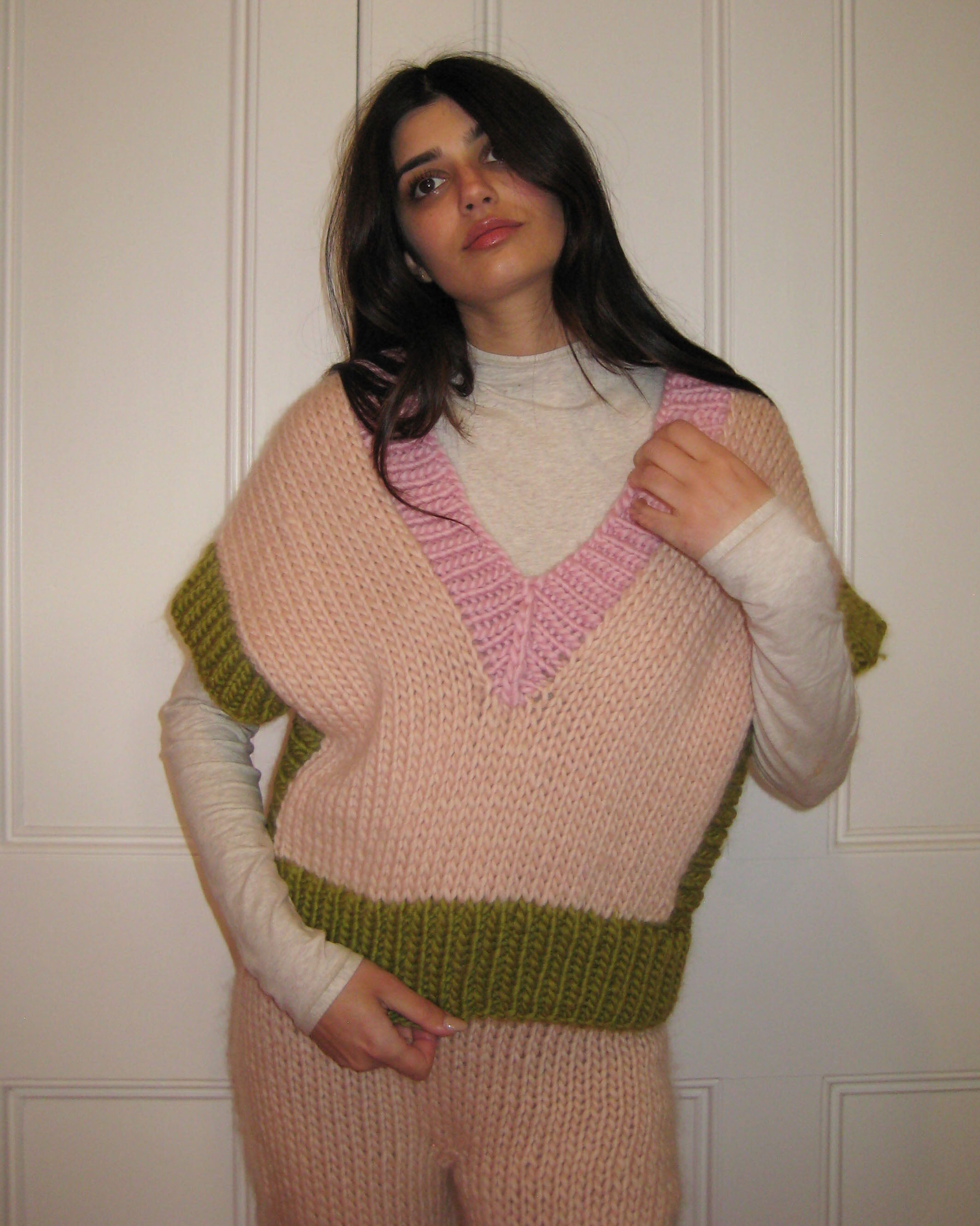A woman in a pink, cream and green vest standing with a white door
