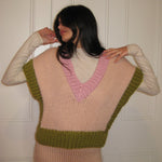 A woman in a pink, cream and green vest standing with a white door