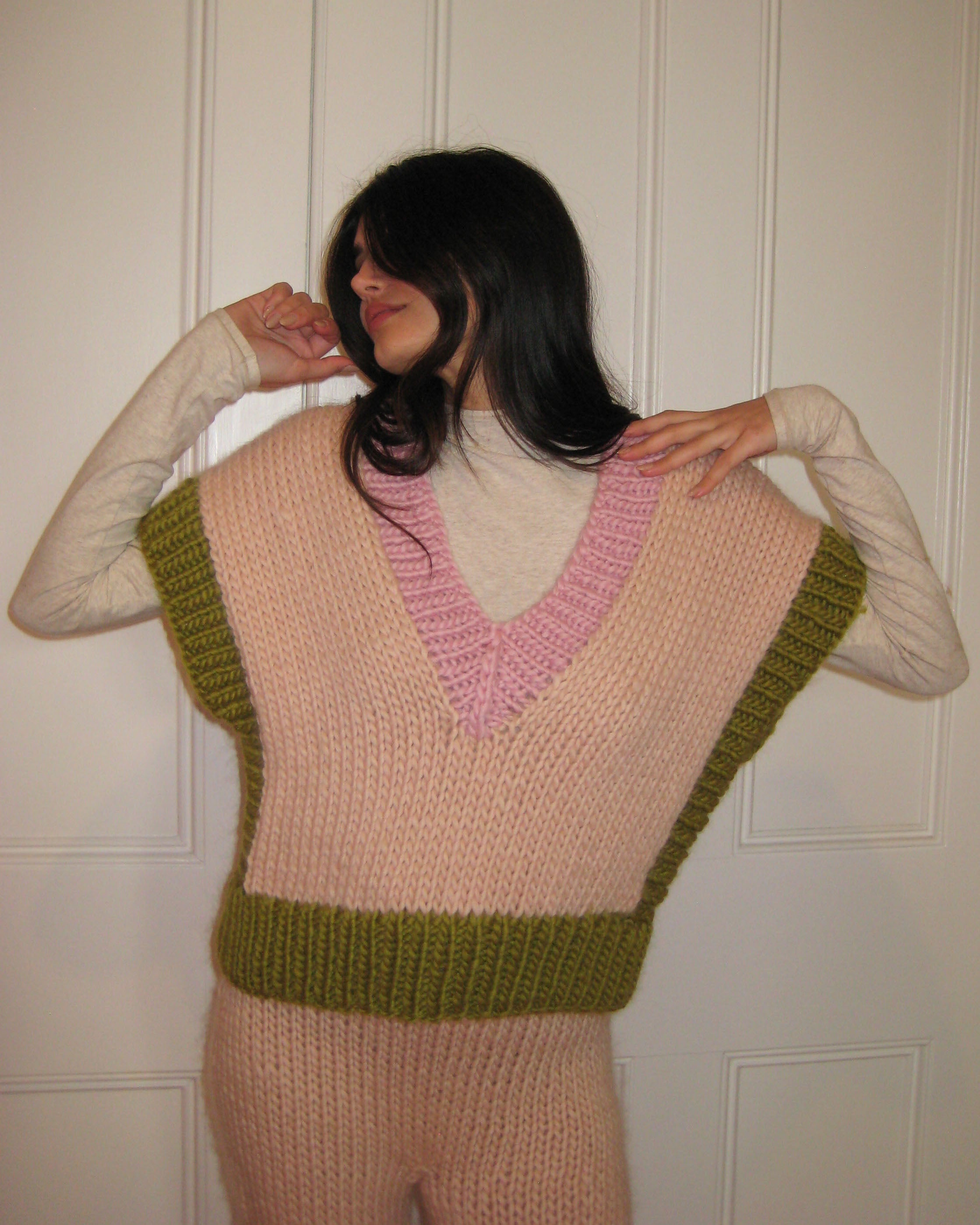 A woman in a pink, cream and green vest standing with a white door
