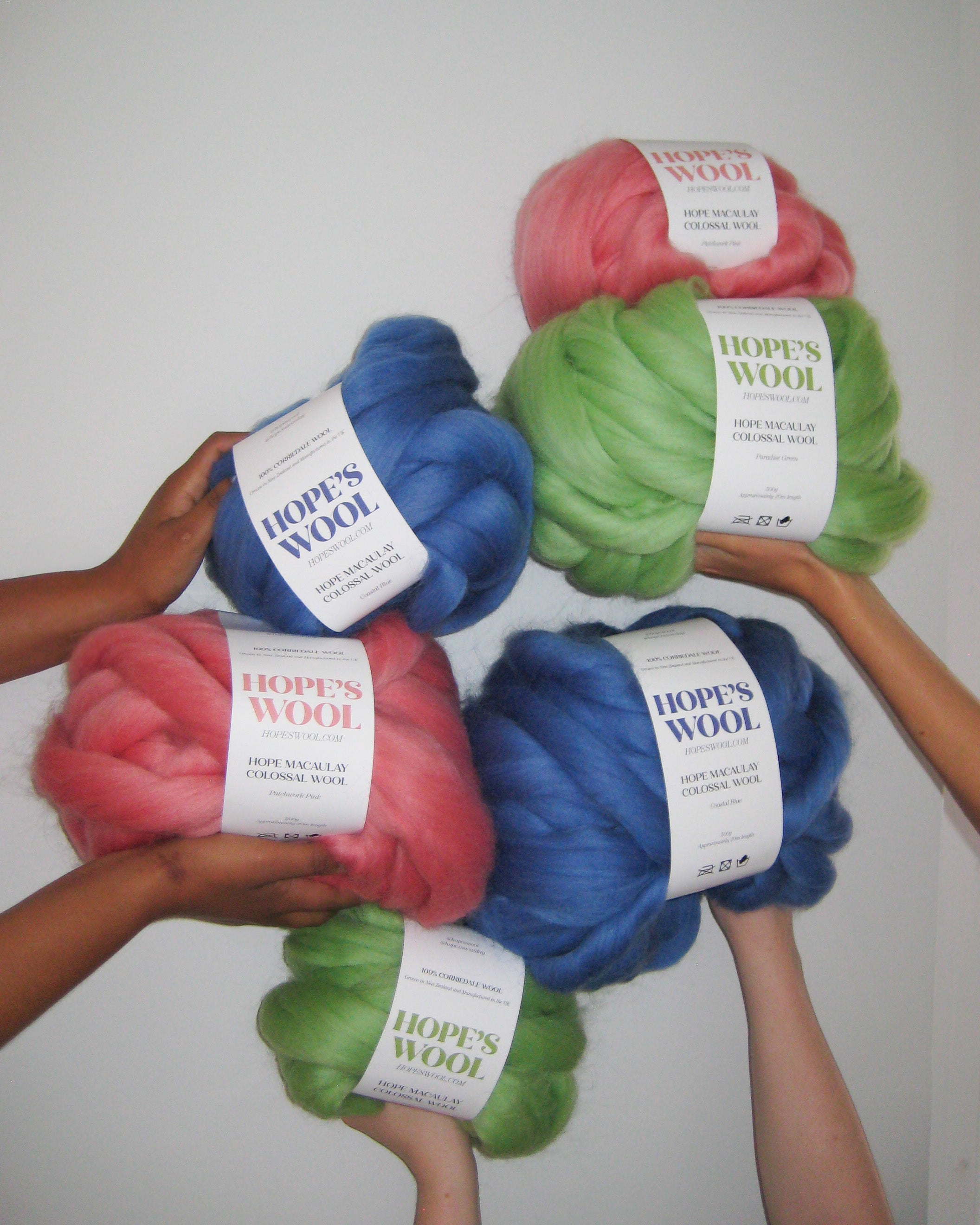 Hands holding up balls of Corriedale wool in Pink, Blue and Green 