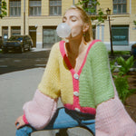 A woman is creating bubbles on a sidewalk wearing a colourful knitted cardigan.