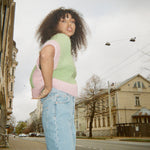 A woman in jeans and a vest posing on a street in a casual and stylish manner.