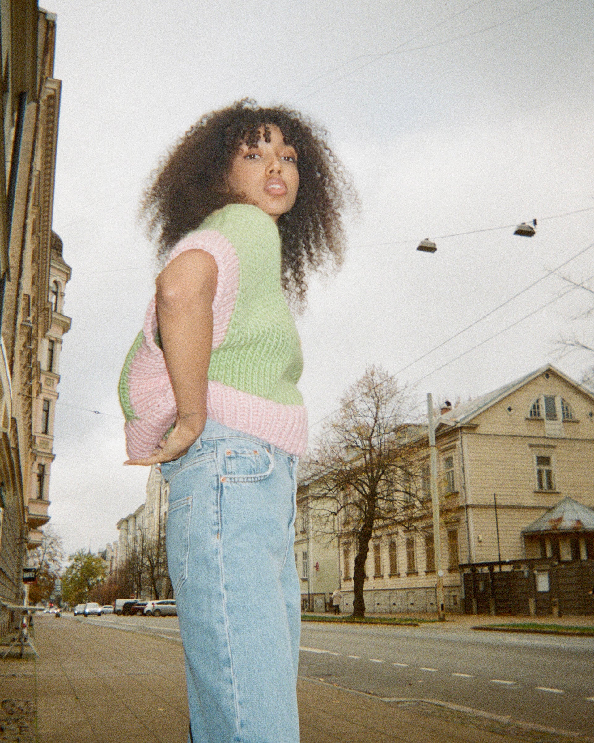 A woman in jeans and a vest posing on a street in a casual and stylish manner.