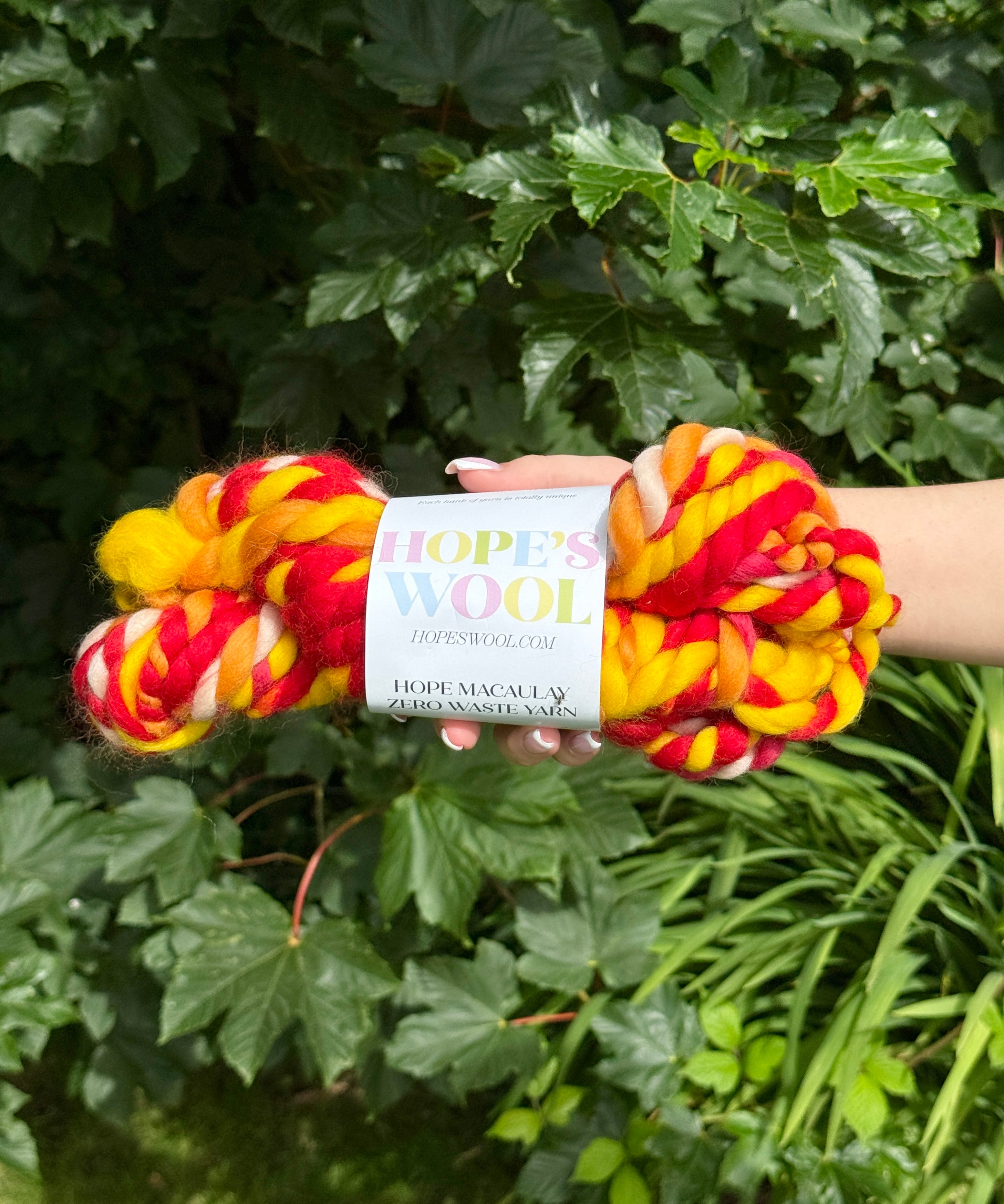 skein of red, yellow, and cream yarn held against a green leafy background