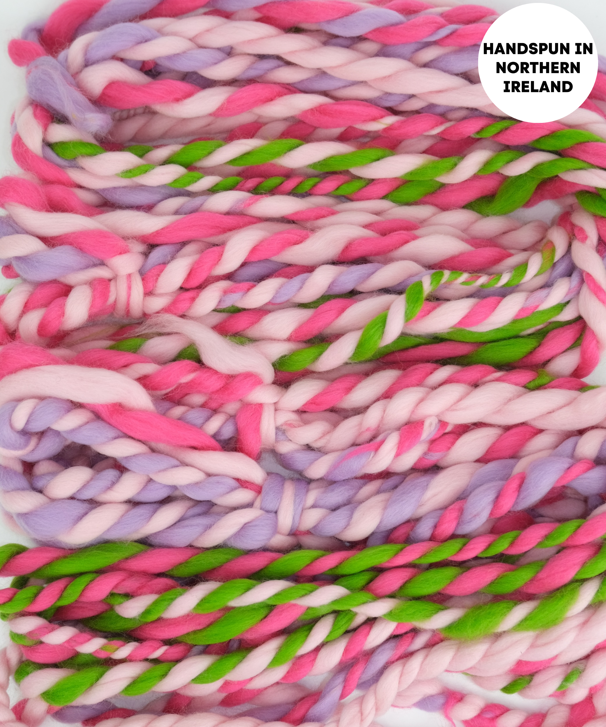 Colorful handspun yarn with pink, green, and purple hues on a white background.
