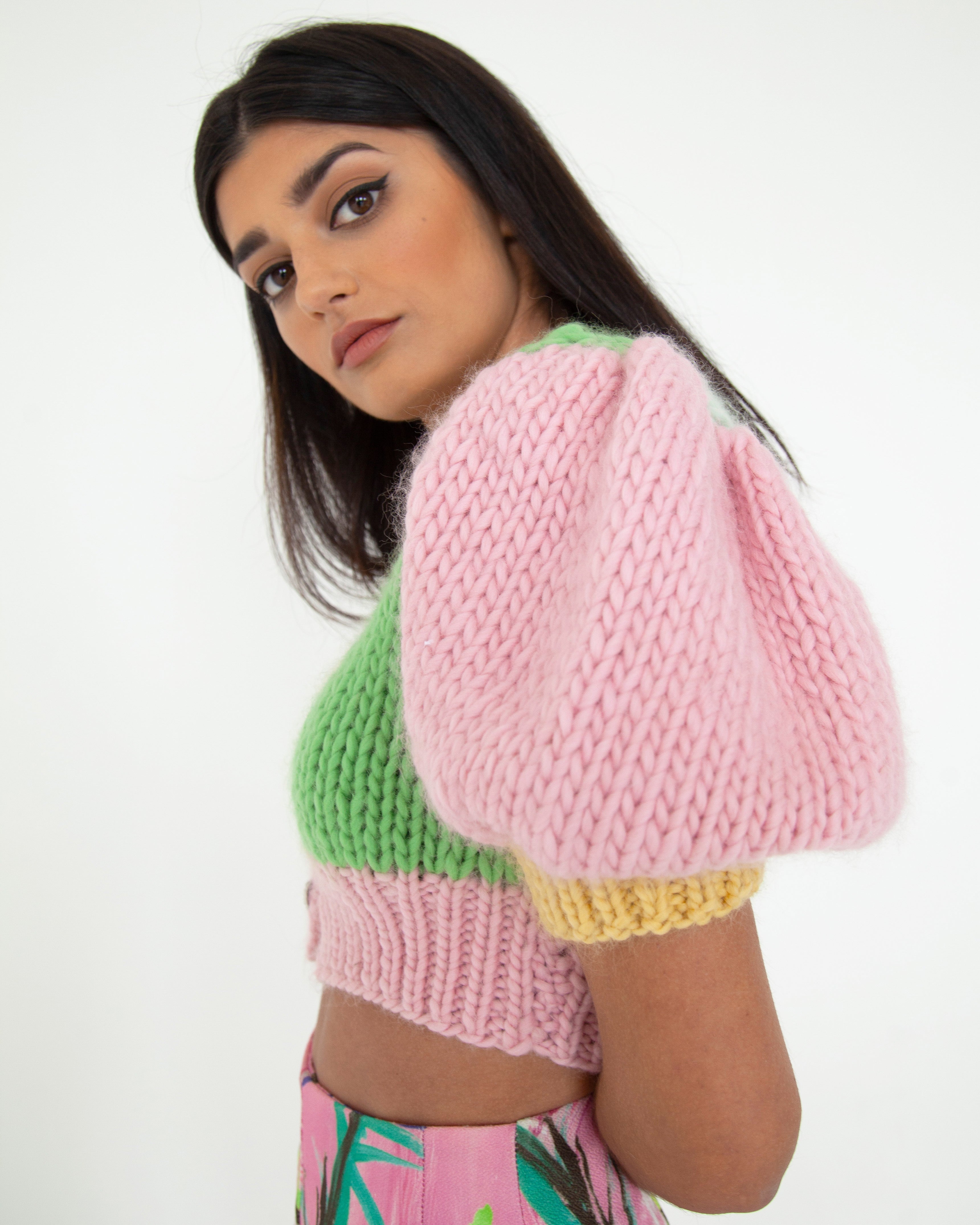 A woman wearing a colourful knitted top in front of a white background