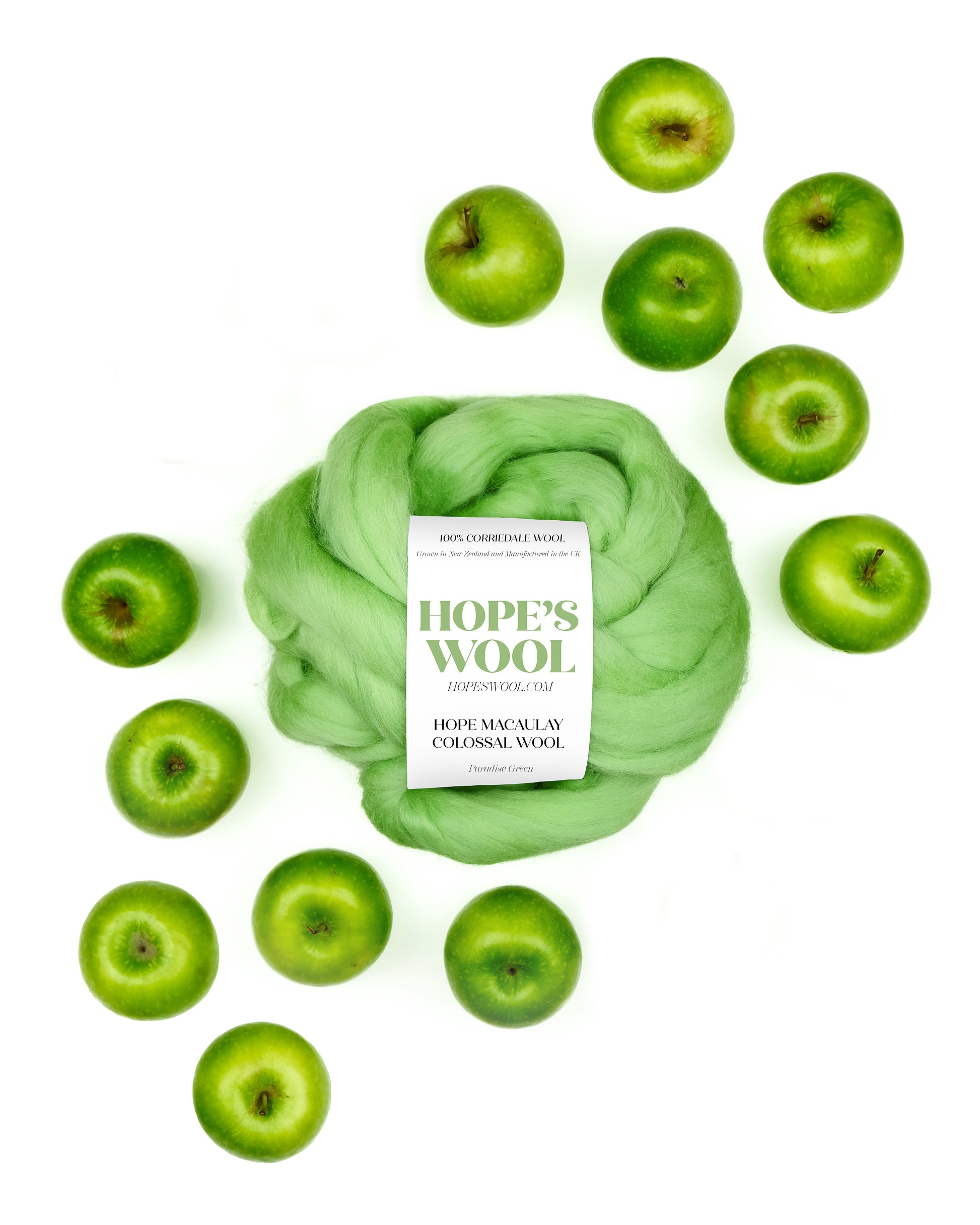 A ball of green Corriedale wool surrounded by green apples