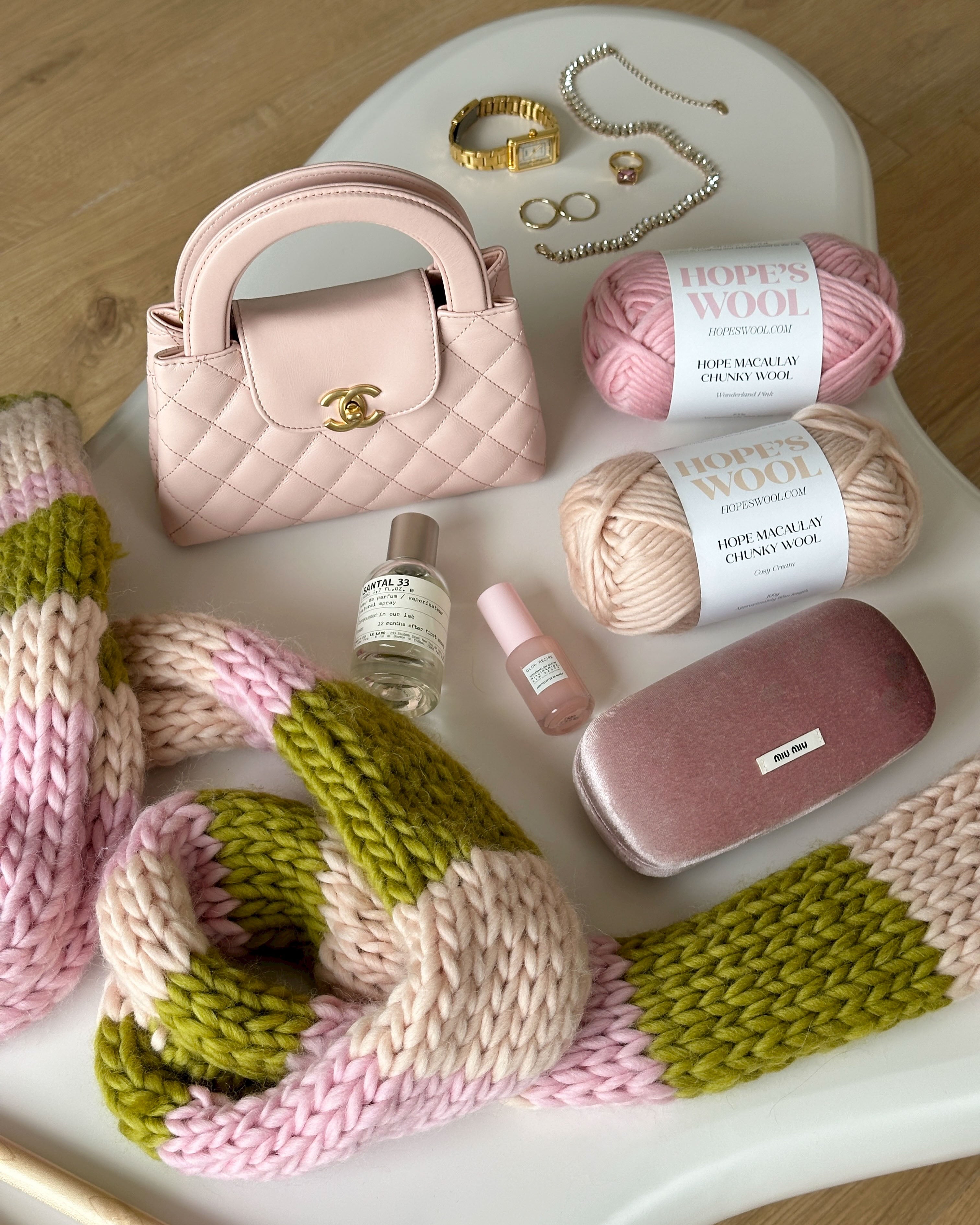 Pink and cream merino wool balls laid on a table beside a colourful knitted scarf