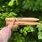 A person holding two wooden knitting needles in front of a bush, ready to start a new knitting project.