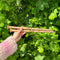 A person holding two wooden knitting needles in front of a bush, ready to start a new knitting project.