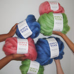 Hands holding up Balls of Corriedale wool in Pink, Blue and Green 