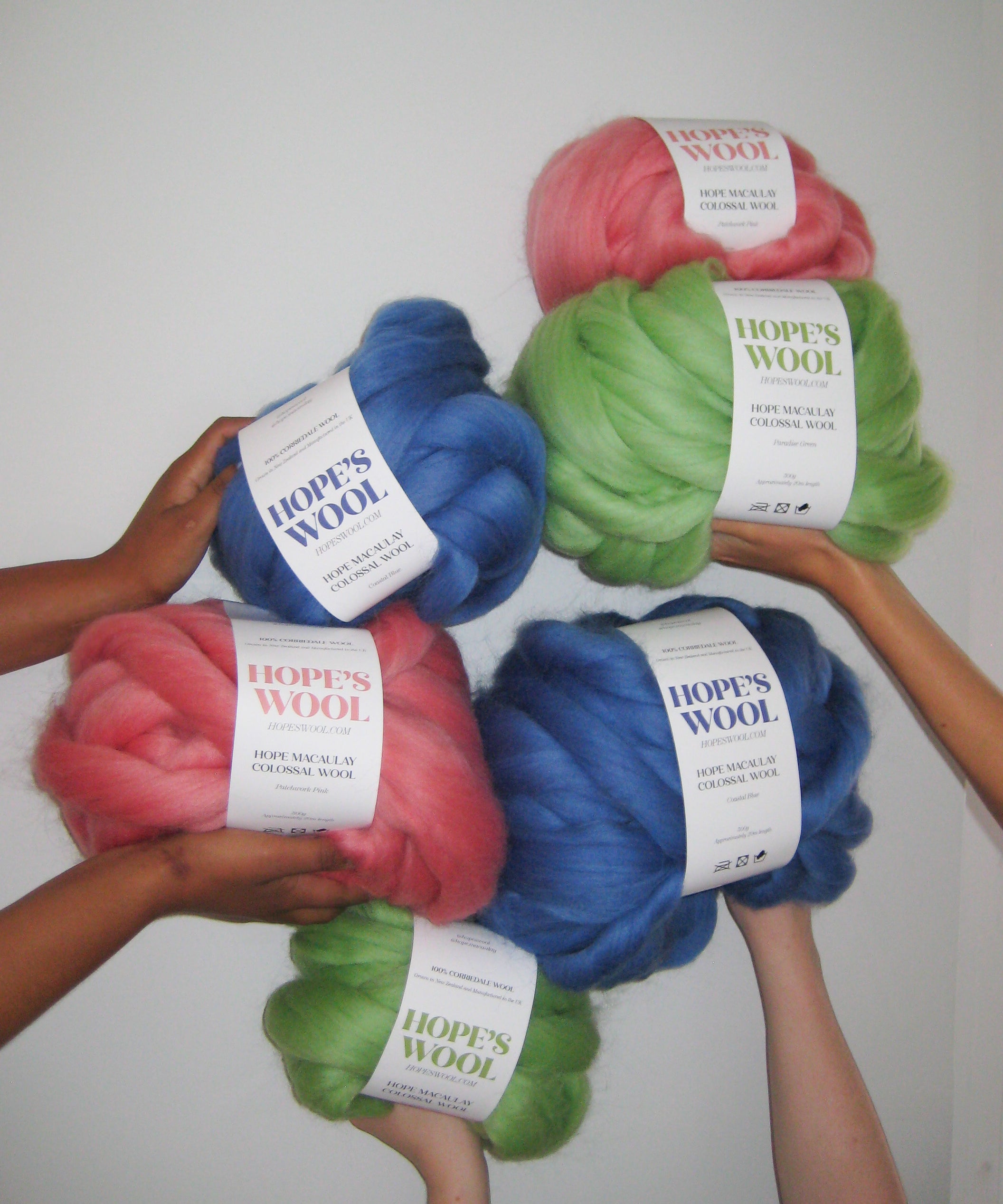 Hands holding up Balls of Corriedale wool in Pink, Blue and Green 