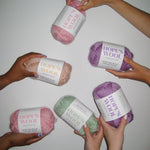 Hands holding up balls of Merino wool in mint, pink, purple and cream