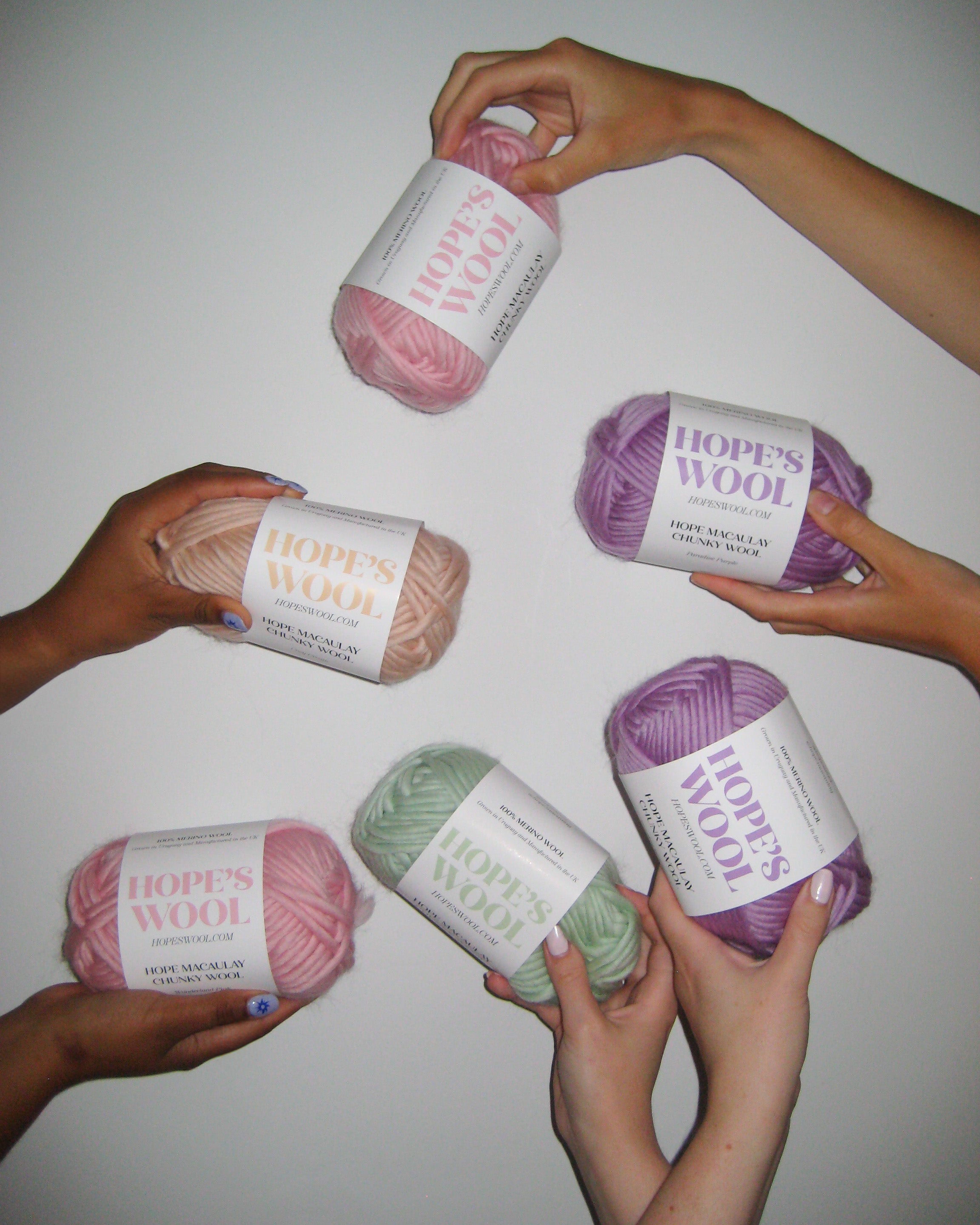 Hands holding up balls of Merino wool in mint, pink, purple and cream