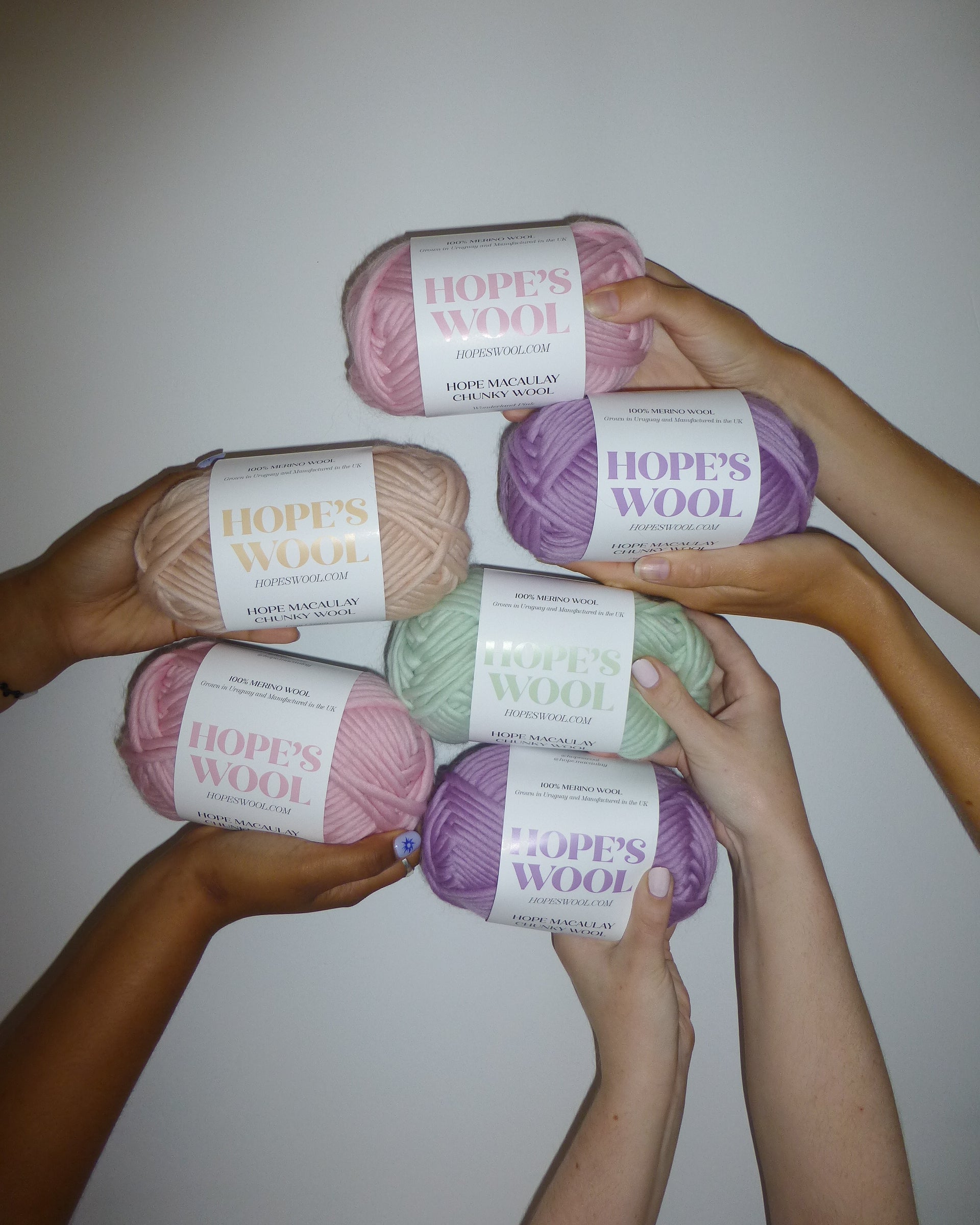 Hands holding up balls of Merino wool in mint, pink, purple and cream