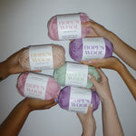 Hands holding up balls of Merino wool in mint, pink, purple and cream 