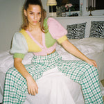 A woman sitting on a bed wearing a colourful knitted top, looking relaxed and cozy.