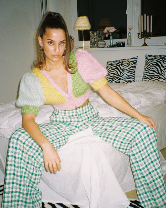 A woman sitting on a bed wearing a colourful knitted top, looking relaxed and cozy.