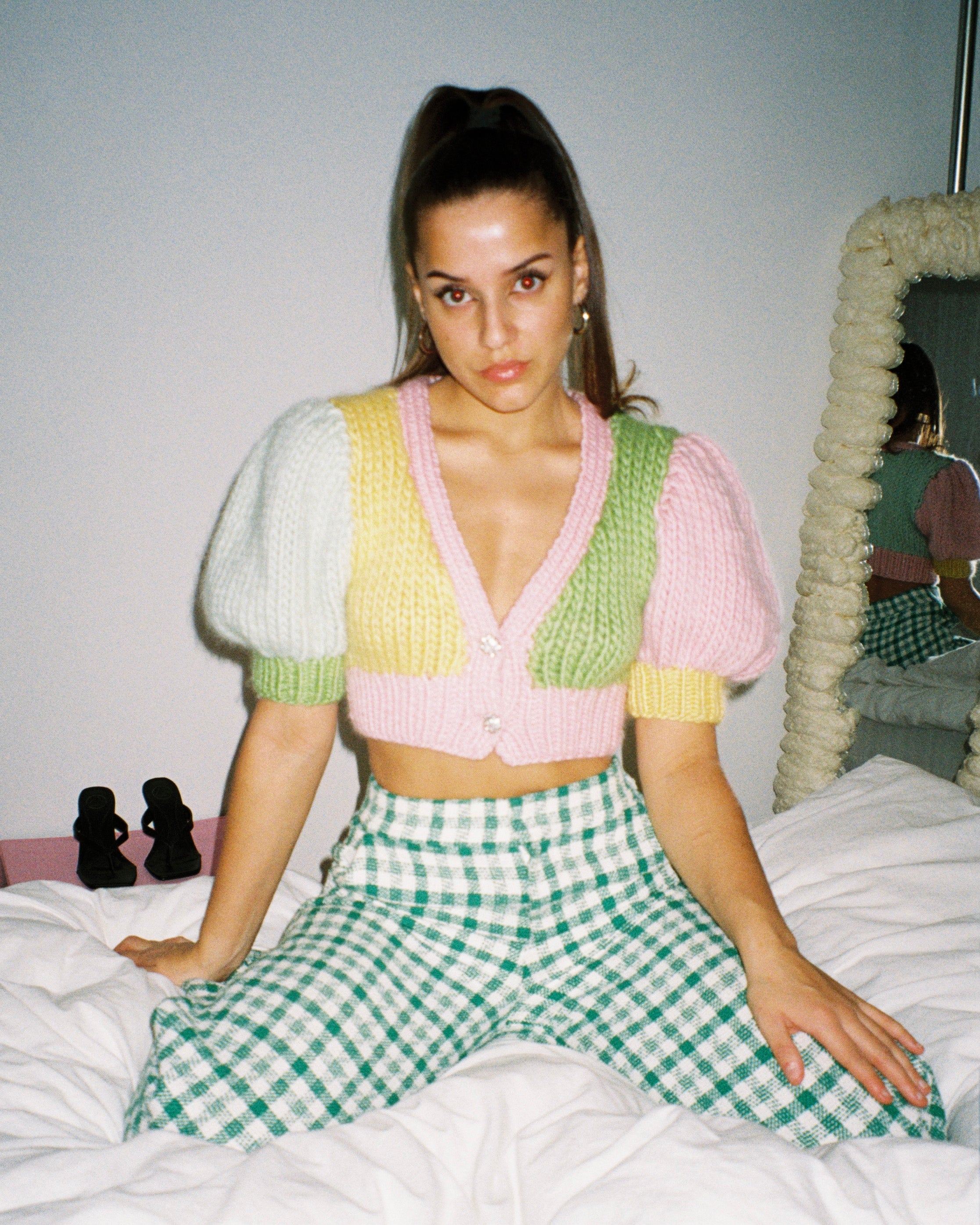 A woman sitting on a bed wearing a colourful knitted top, looking relaxed and cozy.